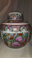 Front view of the hand painted porcelain ginger jar with floral and peach motifs, circular Chinese symbols, and vibrant color palette.