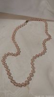 Full view of the antique pink quartz necklace laid out on a white fabric background.