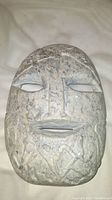 Front close-up of soapstone mask showing flat face, carved eyes, mouth, and patterns on forehead and chin.