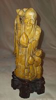 Front view of brown jade statue of an elderly man and child holding peaches on wooden base