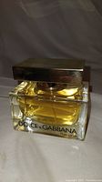 Close-up of rectangular glass bottle with amber liquid and gold rectangular cap, front label 'DOLCE & GABBANA the one'