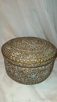 Front view of round hammered copper box with visible Tree of Life medallion on lid and floral patterns on sides.