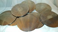 Eight round silver tone hot plates arranged overlapping with visible embossed floral and scroll decorative pattern on the surface. Used condition with slight tarnishing and discoloration.