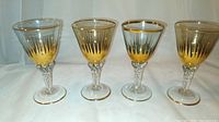 Four hand blown Italian wine glasses with gold painting and twist stems. Two glasses have pale green upper bowl, two have tan color upper bowl. Displayed on white backdrop.