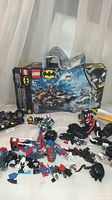 Photo of Lego Batman 76118 box with instruction booklet and multiple disassembled Lego minifigures and pieces spread out including Batcycle parts and figures of Batman, Robin, Mr. Freeze, Spider-Man, and a villain.