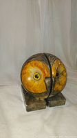 Front view of one round marble owl head bookend showing yellow-orange face with glass eyes and rectangular marble base.