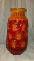Front side view showing bright red and orange vase with textured daisy and diamond patterns.