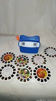 Blue View-Master plastic slide viewer and seven Disney-themed reels spread out around it on a white background. Reels include The Lion King and Handy Manny characters.