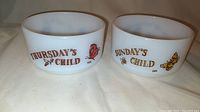 Two vintage FireKing USA milk glass cereal bowls with day-themed titles and colorful butterfly decorations on the front.