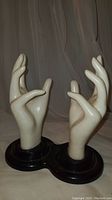 Pair of vintage mannequin display hands mounted on black circular bases, viewed from front showing hand pose and scale.