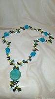 Full view of the necklace laid out showing turquoise stones interspersed with glass/crystal beads and mother of pearl pieces.