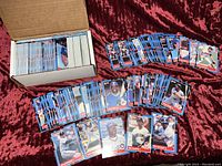 Box filled with approximately 600 1988 Donruss MLB trading cards, with additional cards spread out on red fabric background.