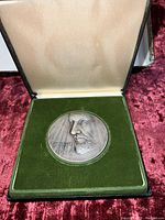 Hinged presentation box open showing obverse of medallion resting in green velvet lining