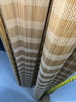 Close-up photo showing natural bamboo slats with white woven pattern in stripes and measuring tape showing about 70 inches length