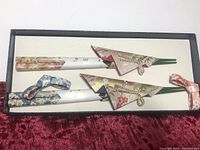Top view of two pairs of Japanese chopsticks with hand-painted decorative sleeves and matching fabric holders in a black box.