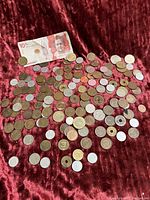 Photo showing a spread of various foreign circulated coins and a 10 unit currency bill on a red velvet surface.