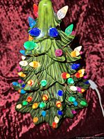 Front view of green ceramic Christmas tree with colorful bulb inserts lit up, placed on red velvet fabric.