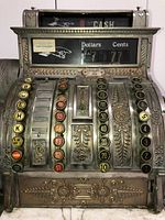 Front view showing cast metal scrollwork, round keys, dollars and cents columns, back cylinder labeled “CASH”