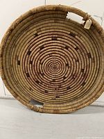 Front view of large circular coil-woven winnowing tray with tight spiral pattern and alternating natural and reddish fiber colors, showing antique wear.