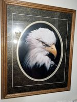 Framed photo showing a close-up of a bald eagle with a dark oval matte and wooden frame.