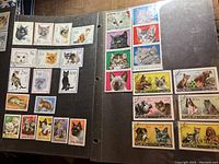 Photo showing stamps predominantly featuring cats with varied color backgrounds in a black album page.