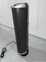 Full view of black upright oscillating air purifier and fan showing cylindrical mesh body, silver top and base, power cord visible on floor.