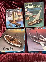 Four vintage wooden ship model kits boxes with front illustrations visible, arranged on red velvet background.