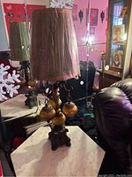 Photo showing one decorative lamp with an ornate base, brown fabric lampshade, globe accents, positioned near the marble top table and sofa.