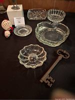 Five glass ashtrays, pilot figurine, large key bottle opener, mouse ball toy on a black surface with wooden background