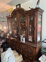 Photo of large wooden display cabinet showing front and side views with glass paneled doors and multiple shelves.