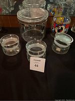 Set of three clear glass canisters of small, medium, and large sizes with airtight lids, placed together with a Looney Tunes themed glass vase/jug decorated with colorful cartoon characters.