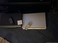Photo showing silver Panasonic DVD player and black VCR player with their respective remotes on top.