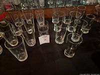 Multiple angles showing 18 pieces of clear glassware including tall glasses, short glasses, and shot glasses on a black surface with mirror background.