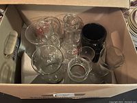 Top down view of assorted glassware inside cardboard box showing various sizes and designs.