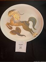 Photo of the mid century circular tray showing a stylized leaping horse design in gold and blue hues on a white background.