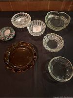 Photo of seven mixed glass ashtrays arranged on a black surface.