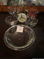Set of glass mixing bowls, measuring cup, pie dish, and white measuring funnel arranged on black surface.