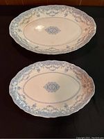 Two oval Royal semi-porcelain Blue Como serving plates displayed on a black surface showing floral blue pattern and scalloped edging.