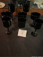 Eight black vintage glass goblets on black surface with a mirror background.