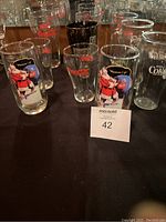 Photo showing various Coca-Cola glasses including vintage Santa Claus designs and classic logos. Includes both tall and short glasses and a black straw dispenser.