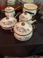 Five piece vintage ceramic cookware set with floral pattern, various sizes and shapes including saucepans and casserole dishes, with lids and brass-tone knob handles.