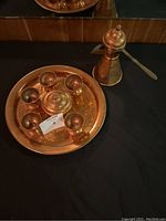 Top view of the brass/copper tea set showing six cups, a lidded sugar bowl, and a large round engraved tray with a tall coffee pot to the side.
