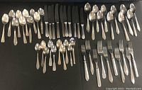 Top-down view showing the full set of cutlery including knives, forks, and spoons arranged by type on a black surface.