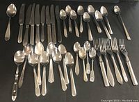 Photo showing the full assortment of 36 cutlery pieces arranged on a dark surface, including knives, forks, and various spoons.