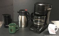 Photo showing Hamilton Beach coffee maker, collector coffee thermos, Proctor Silex coffee mill, and two coffee mugs (green and beige)