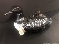 Front view of the northern loon figurine with baby loon seated on back, showing detailed black and white paint with red eyes and felt base underneath.