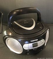 Black Toshiba portable AM/FM radio CD player model TY-CW59 with front digital display and Bluetooth logo, built-in handle, silver speaker grills on sides.