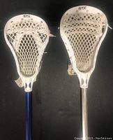 Top view showing the heads of both lacrosse sticks, white plastic heads with mesh pockets, branded STX.