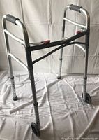 Silver collapsible walker with two front wheels and black rubber hand grips, showing front and side view.