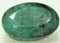 Close-up photo of the oval faceted green emerald gemstone showing internal inclusions and color variations.